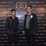 Two well dressed men standing in front of an awards backdrop.