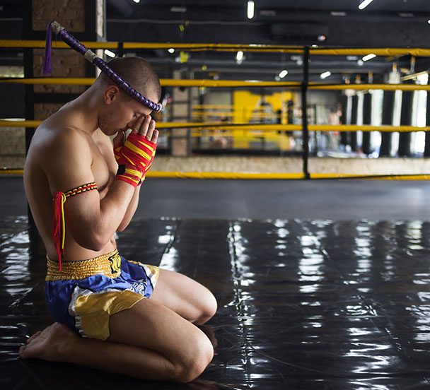 Muay Thai fighter kneeling to pray ringside.